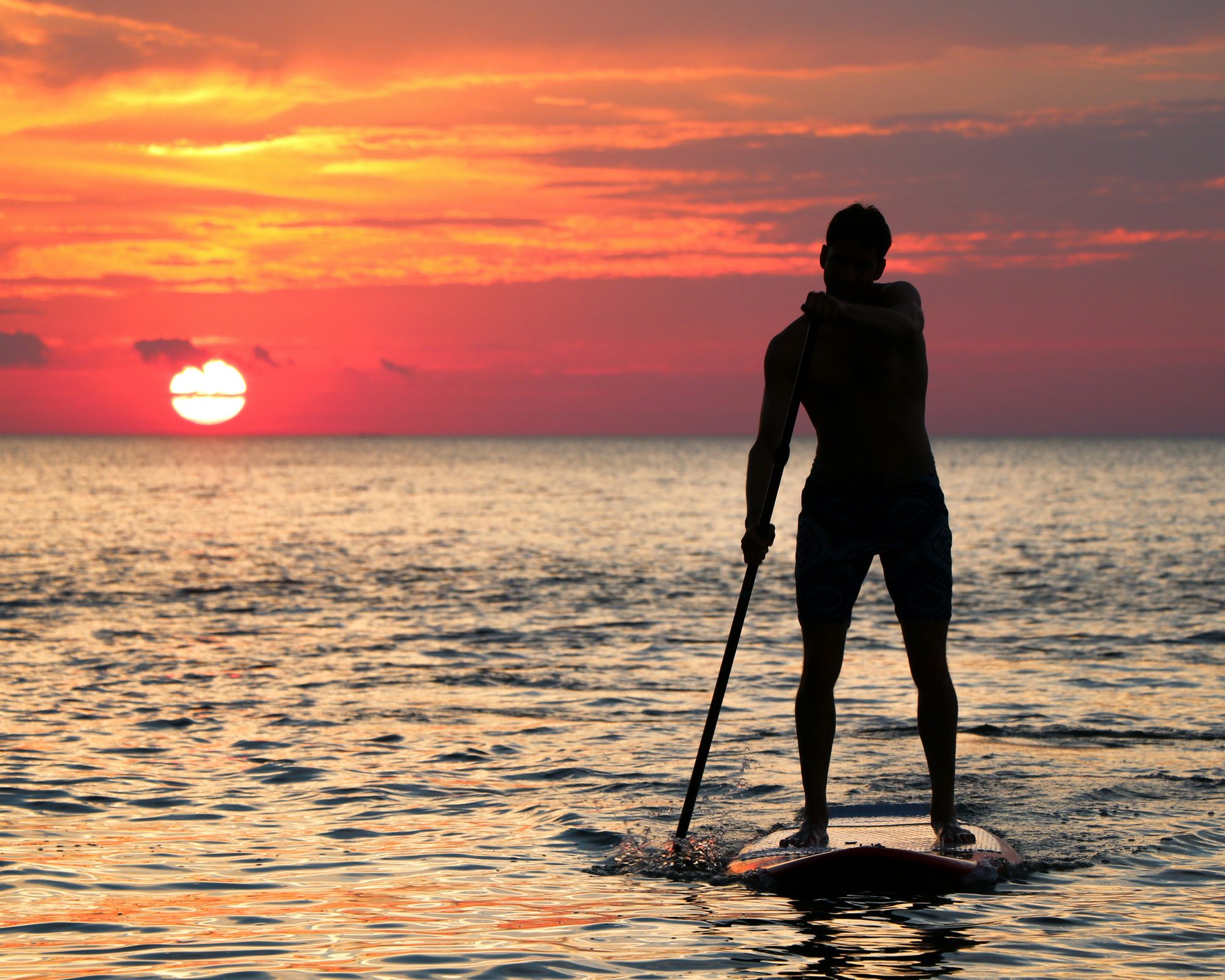 Paddleboarder gliding across the water at sunset